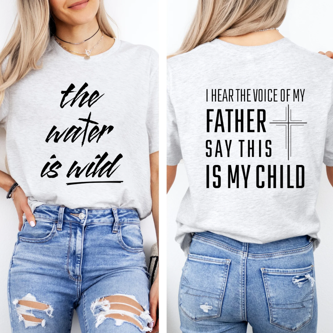 Ash white crewneck t-Shirt that says, “the water is wild”. The “t” in water is a cross. The back says, “I hear the voice of my father say this is my child” with a large cross in the middle.