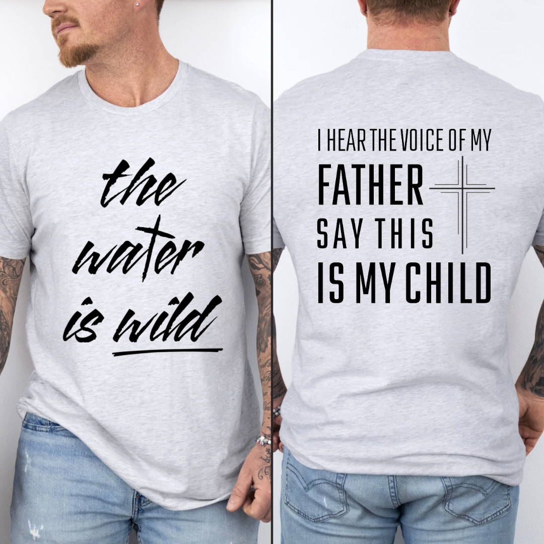 Ash white crewneck t-Shirt that says, “the water is wild”. The “t” in water is a cross. The back says, “I hear the voice of my father say this is my child” with a large cross in the middle.