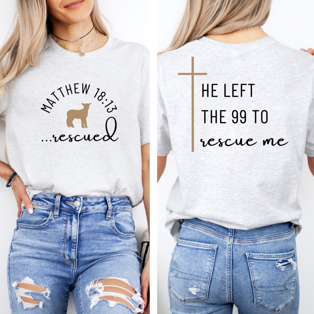 Ash white crewneck T-Shirt that says, "He left the 99 to rescue me" with a large tan cross. On the front it says, "Matthew 18:13 rescued" with a tan sheep. 