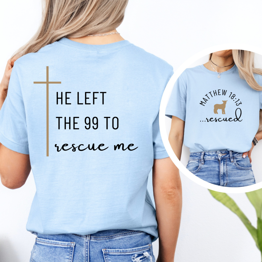 Baby blue crewneck T-Shirt that says, "He left the 99 to rescue me" with a large tan cross. On the front it says, "Matthew 18:13 rescued" with a tan sheep. 