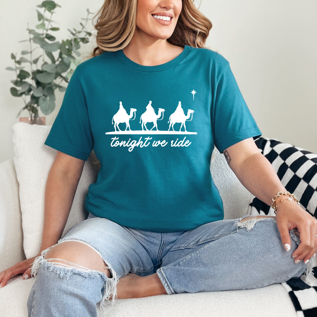 Deep teal crewneck t-shirt that says, “tonight we ride” with an image of the three wisemen riding on camels towards the Christmas star.