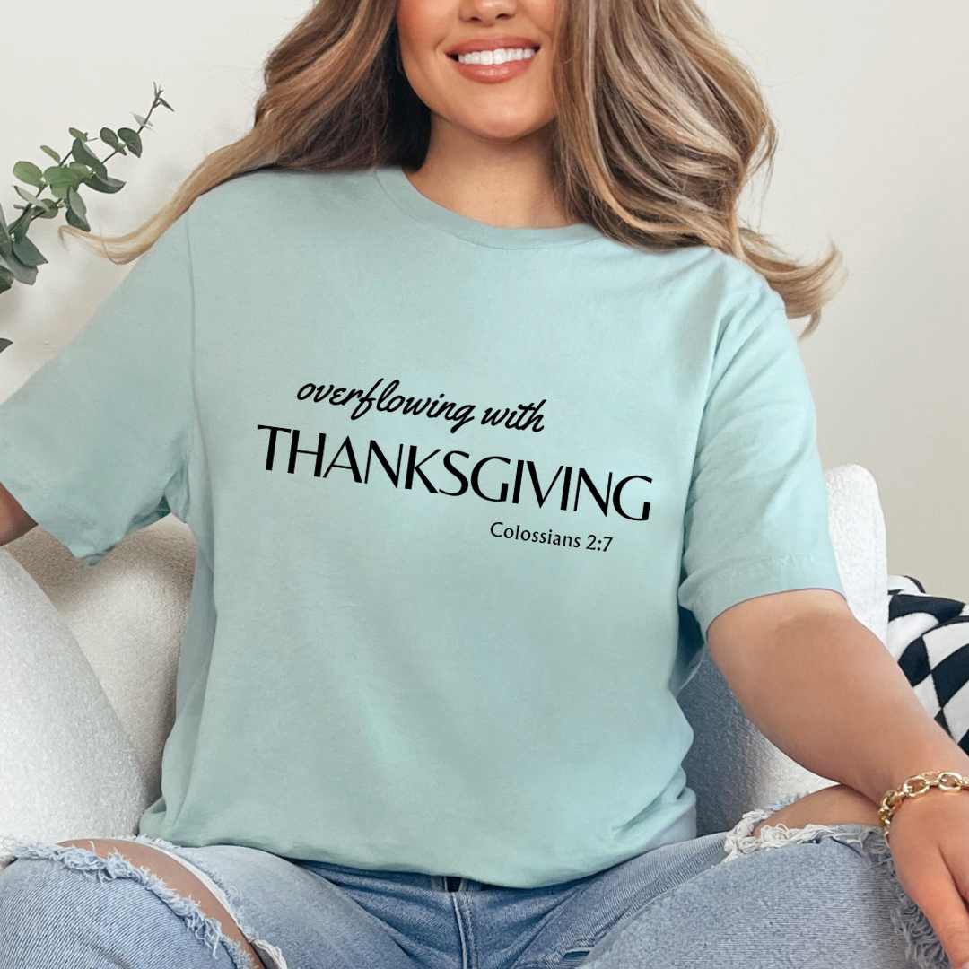 Dusty green crewneck t-shirt that says, "overflowing with thanksgiving. Colossians 2:7." 