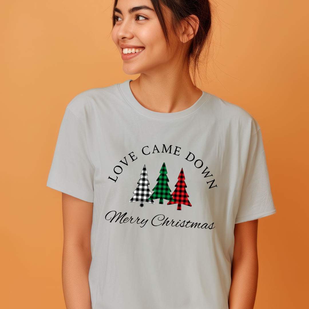 Grey crewneck t-shirt that says, "Love came down. Merry Christmas." It features 3 Christmas trees in buffalo plaid green, red and white.