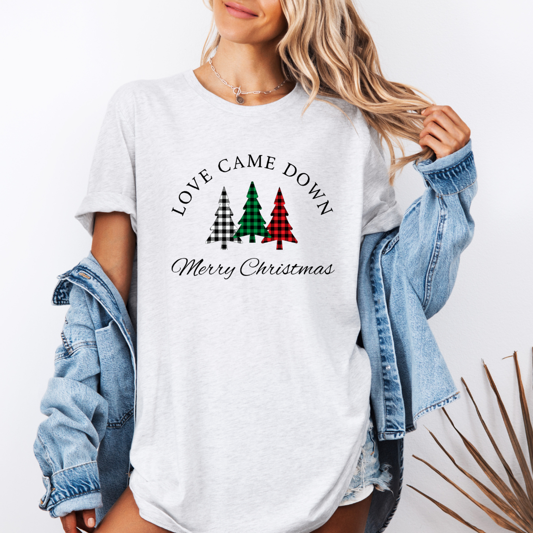 Ash white crewneck t-shirt that says, "Love came down. Merry Christmas." It features 3 Christmas trees in buffalo plaid green, red and white.