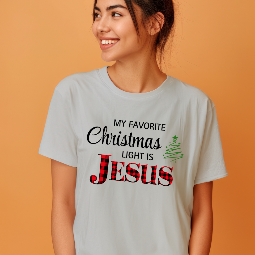 Grey crewneck t-shirt that says, "My favorite Christmas light is Jesus." Jesus is in red buffalo plaid, there is a Christmas tree graphic.