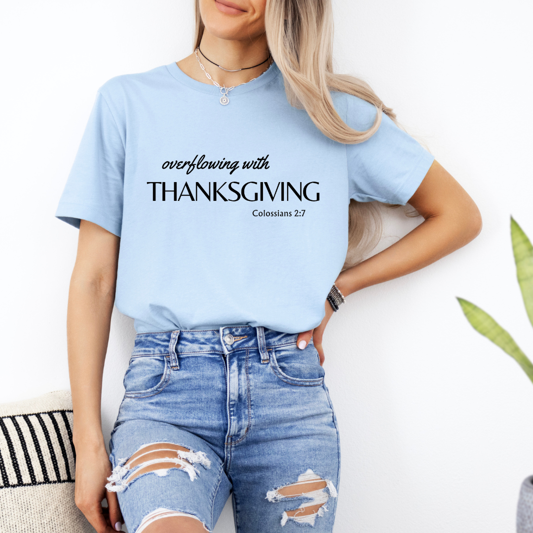 Baby blue crewneck t-shirt that says, "overflowing with thanksgiving. Colossians 2:7." 