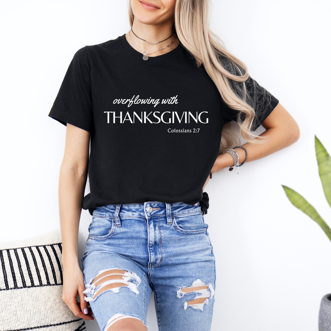 Black crewneck t-shirt that says, "overflowing with thanksgiving. Colossians 2:7." 